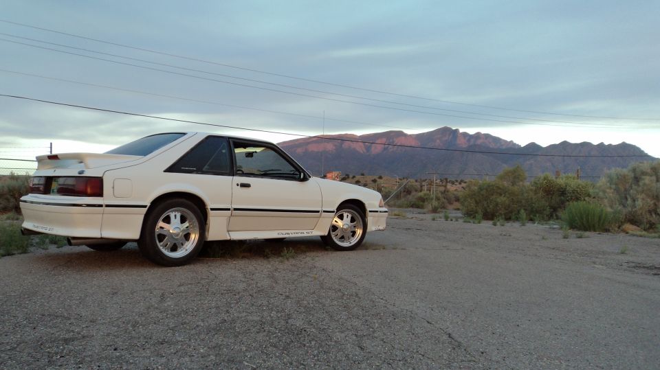 1989 Ford Mustang coupe parked on a dirt road with mountains in the background