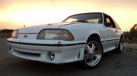 1989 Ford Mustang - White 1989 Ford Mustang GT with aftermarket wheels parked on a dirt road during sunset.