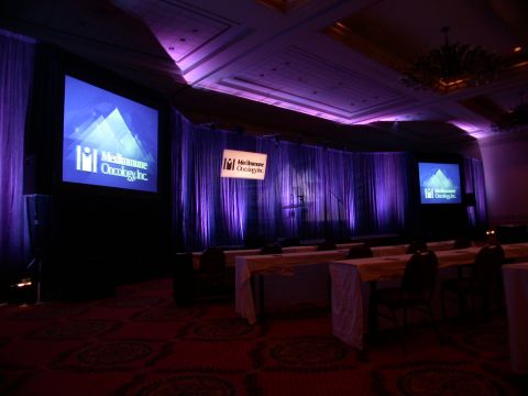 1994 Ford Bronco - A conference room is set up with tables and chairs, illuminated by purple lighting and screens with the MedImmune Oncology Inc. logo.