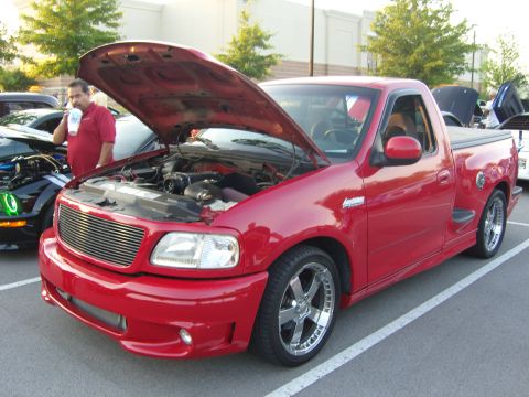 2007 Ford Mustang - A man stands by a red pickup truck with its hood open, parked next to another vehicle.
