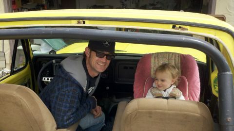 1978 Ford Bronco - A man and a baby are inside the interior of a yellow 1978 Ford Bronco, with the baby secured in a car seat.