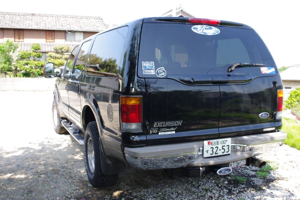Rear 3/4 view of a black Ford Excursion SUV with Japanese plate on gravel
