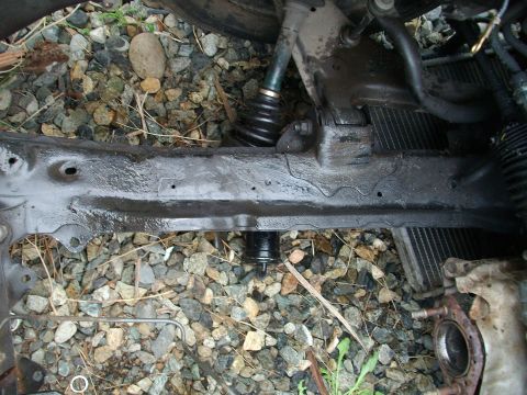 1989 Ford Probe - Close-up of a vehicle's subframe and suspension components, resting on gravel.