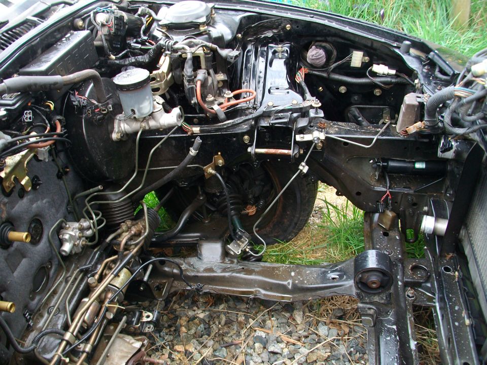 Car engine bay with brake master cylinder and various hoses and wiring. Some parts removed