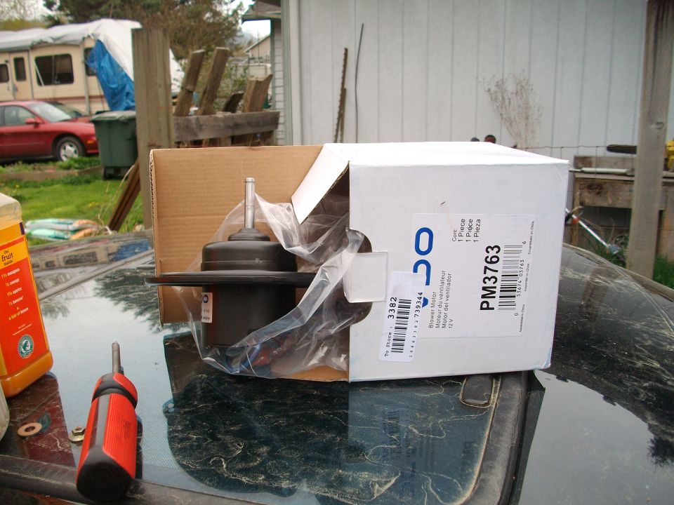 Blower motor part in box with screwdriver and bottle on a dark surface