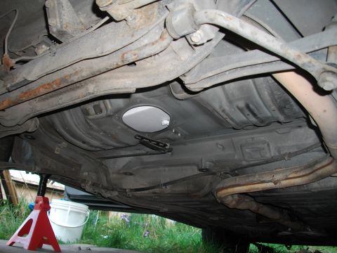 1989 Ford Probe - The undercarriage of a vehicle is visible, supported by jack stands, with grass and a bucket in the background.
