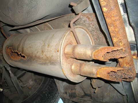 1989 Ford Probe - The underside of a vehicle shows a heavily rusted dual exhaust system with a damaged muffler.