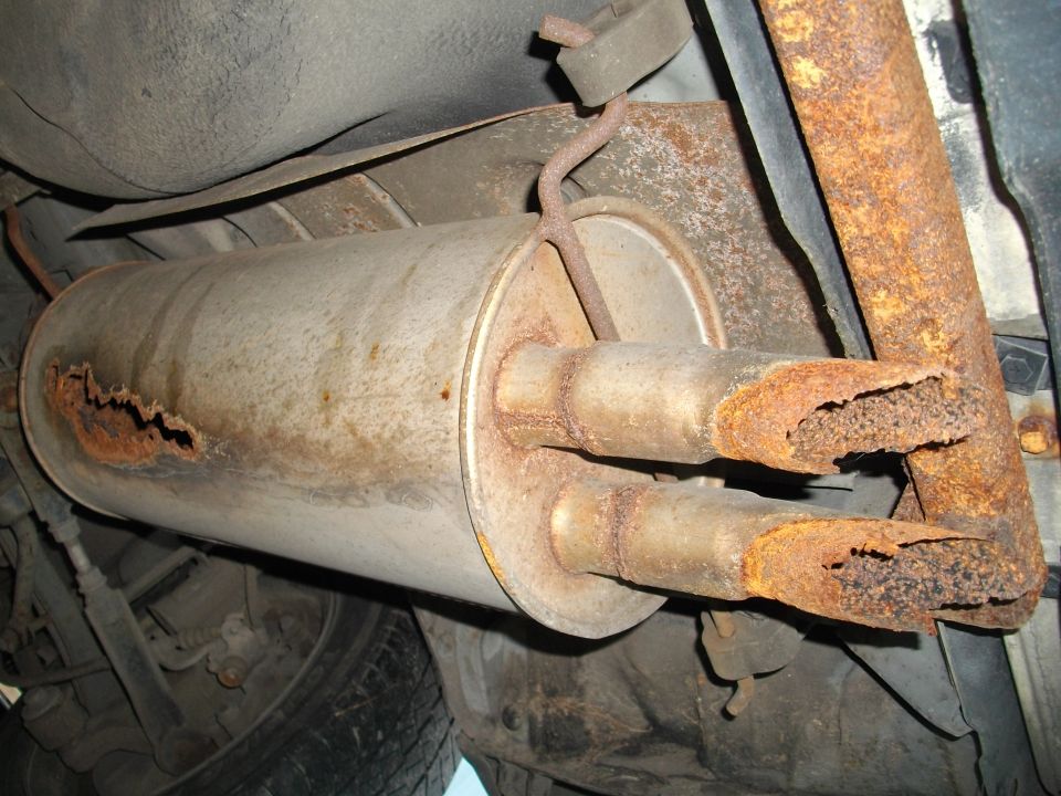 Dual exhaust pipes on a rusty muffler, viewed from below