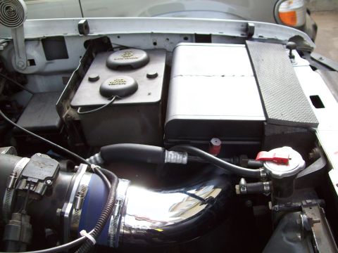 1993 Ford F-150 - Engine bay of a 1993 Ford F-150, showing the battery, coolant reservoir, and a chrome intake pipe.