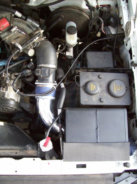 1993 Ford F-150 - Engine bay view of a 1993 Ford F-150, a chrome intake pipe and various fluid reservoirs.