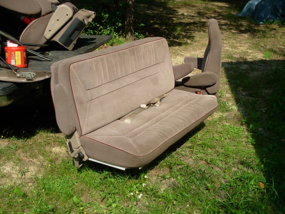 Tan cloth bench seat with red piping sitting on grass outdoors