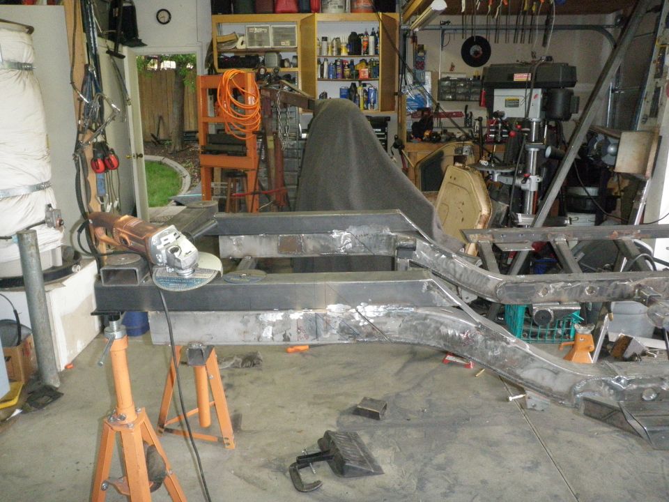 Modified vehicle frame on jack stands with an angle grinder nearby in a garage