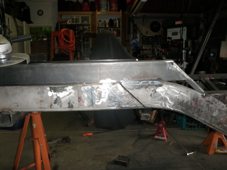 Close-up of a metal frame section with weld marks and chalk lines, supported by jack stands in a workshop