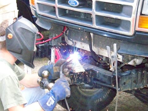1985 Ford Bronco - A person welds a metal piece onto the front bumper of a Ford truck, with sparks flying.