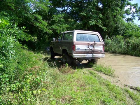 1985 Ford Bronco - This 1985 Ford Bronco navigates a muddy trail surrounded by lush greenery.