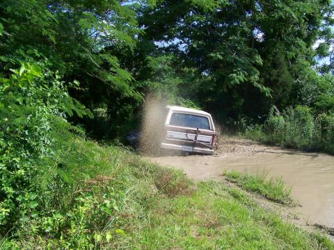 1985 Ford Bronco - A Ford Bronco navigates a water-filled trail, sending mud and water flying.