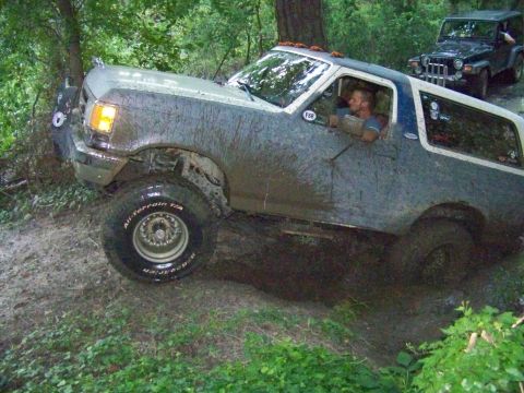 1985 Ford Bronco - This lifted SUV navigates a muddy trail, with a Jeep visible in the background.
