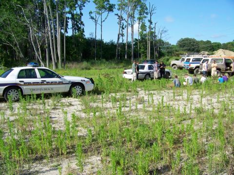 1985 Ford Bronco - Several vehicles, including police cars and off-road SUVs, are gathered in a field with a group of people.