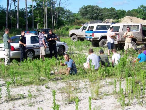 1985 Ford Bronco - Several people gather around a police car and off-road vehicles in a grassy area.