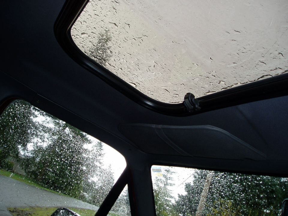view through car sunroof with rain drops, trees and houses outside