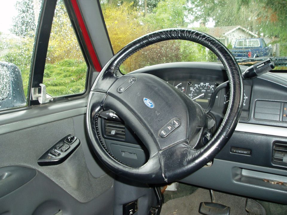 Ford steering wheel and dashboard with a blue truck visible through the window