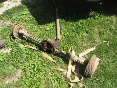 1987 Jeep Comanche - An old vehicle axle assembly with its differential exposed and a brake drum attached rests on the grass.