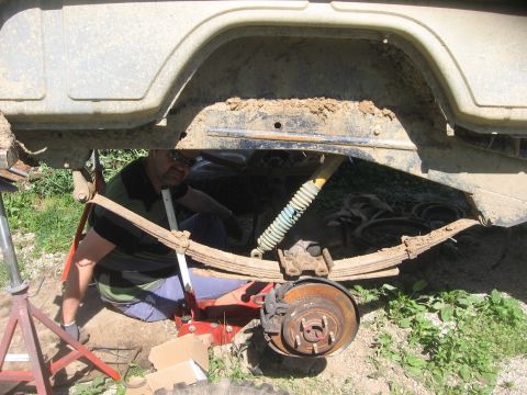 1987 Jeep Comanche - A mechanic works on the rear axle suspension of a vehicle, focusing on leaf springs and a shock absorber.