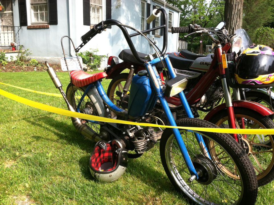 Blue moped with red seat and chrome exhaust next to a red moped with a helmet on it