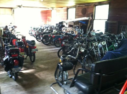 1981 Garelli Rally Sport - A large collection of mopeds are stored inside a rustic wooden garage.