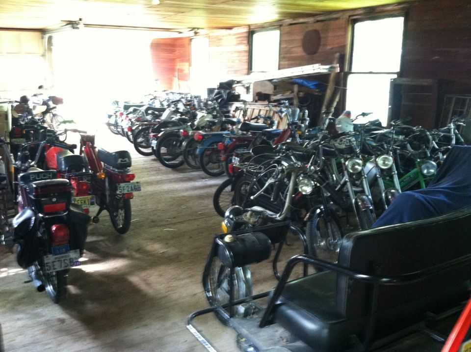 Interior of a cluttered garage filled with many mopeds parked closely together