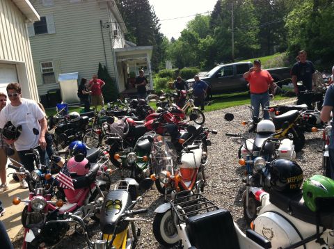 1981 Garelli Rally Sport - A gathering of various mopeds and motorcycles is shown parked in a gravel lot next to a building.