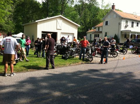 1981 Garelli Rally Sport - A gathering of people and motorcycles in front of a garage and residential buildings.