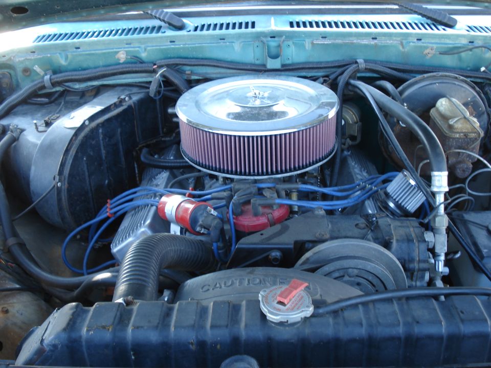 Engine bay showing a large round air filter, distributor cap, and radiator. Text on radiator reads 'CAUTION'