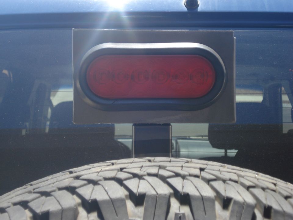 Aftermarket red oval LED third brake light mounted above spare tire on rear of blue SUV