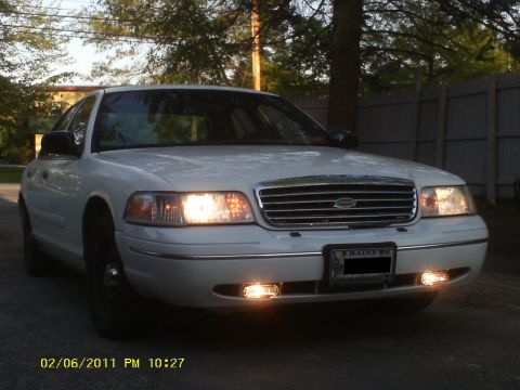 1998 Ford Crown Victoria - This sedan features a prominent chrome grille and illuminated headlights, parked outdoors.