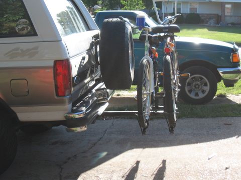 1994 Ford Bronco - Rear view of a Ford Bronco with a spare tire and bicycle rack, parked next to a green pickup truck.