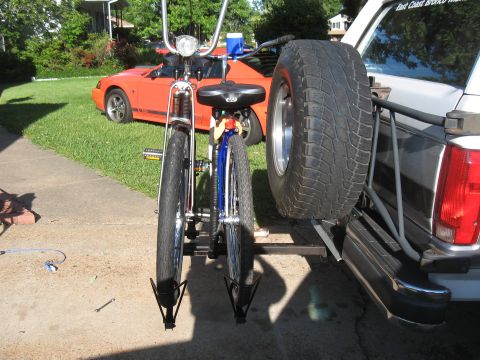 1994 Ford Bronco - A white SUV carries two bicycles on its rear rack, parked near a red sports car.