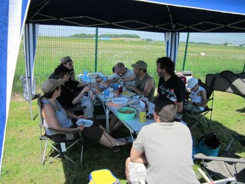 1991 Ford LTD Crown Victoria - A group of people enjoy a meal outdoors under a tent, with a wide open field visible behind them.