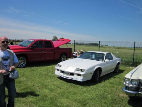 1991 Ford LTD Crown Victoria - A white 1980s sports coupe and a red pickup truck are parked on a grassy field under a blue sky.