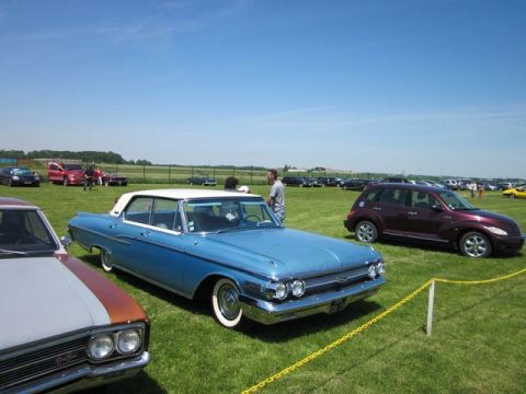 1991 Ford LTD Crown Victoria - A blue vintage sedan is parked on a grassy field with other vehicles and people around.