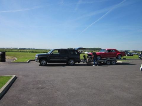 1991 Ford LTD Crown Victoria - A black SUV tows a red coupe on a trailer under a clear blue sky.