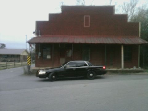 2004 Ford Crown Victoria - A black 2004 Ford Crown Victoria is parked in front of a rustic building.