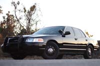 2004 Ford Crown Victoria - A black 2004 Ford Crown Victoria police car is parked outdoors with trees in the background.