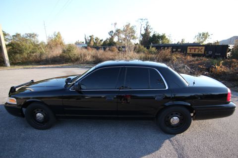 2004 Ford Crown Victoria - A black 2004 Ford Crown Victoria sedan is parked on the side of the road with a train car visible in the background.
