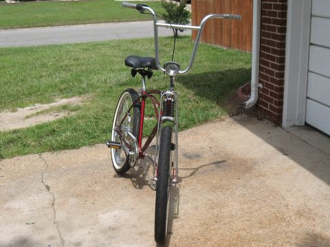 1994 Ford Bronco - Cruiser bicycle with chrome handlebars and a red frame sits on a driveway next to a brick garage.