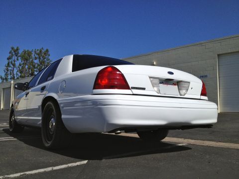 2004 Ford Crown Victoria - The rear of a white sedan is shown parked in front of a commercial building under a clear blue sky.