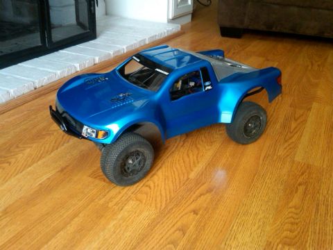 1986 Ford Bronco - A blue RC truck sits on a polished wood floor near a white brick fireplace.