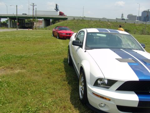 2007 Ford Mustang - Two Ford Mustangs are parked on a grassy area near an overpass.