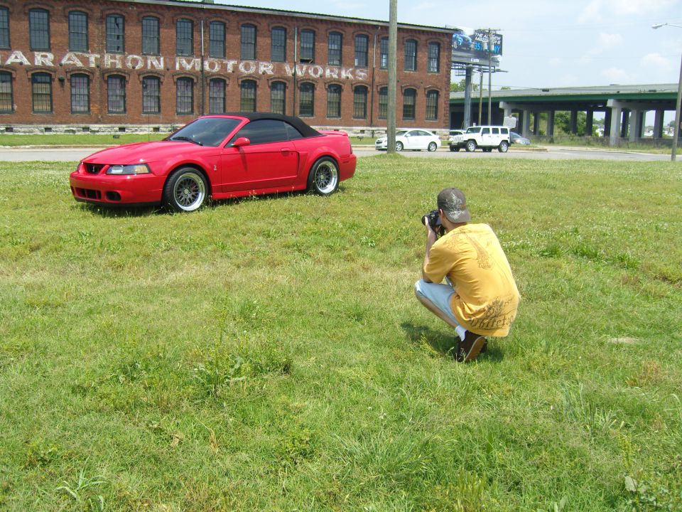 Red convertible Mustang parked on grass, photographer crouching nearby