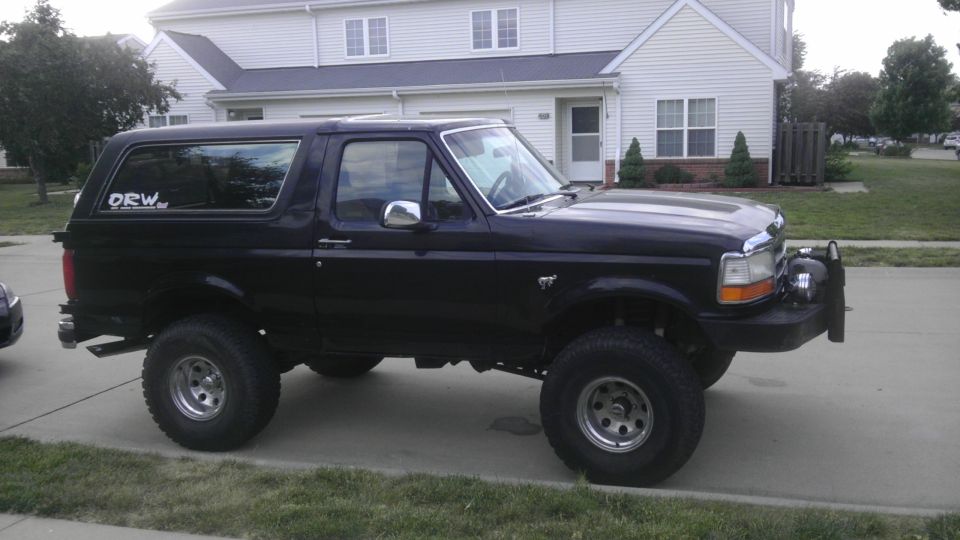 Black Ford Bronco parked in driveway, lifted with off-road tires. Has a sticker on the rear window